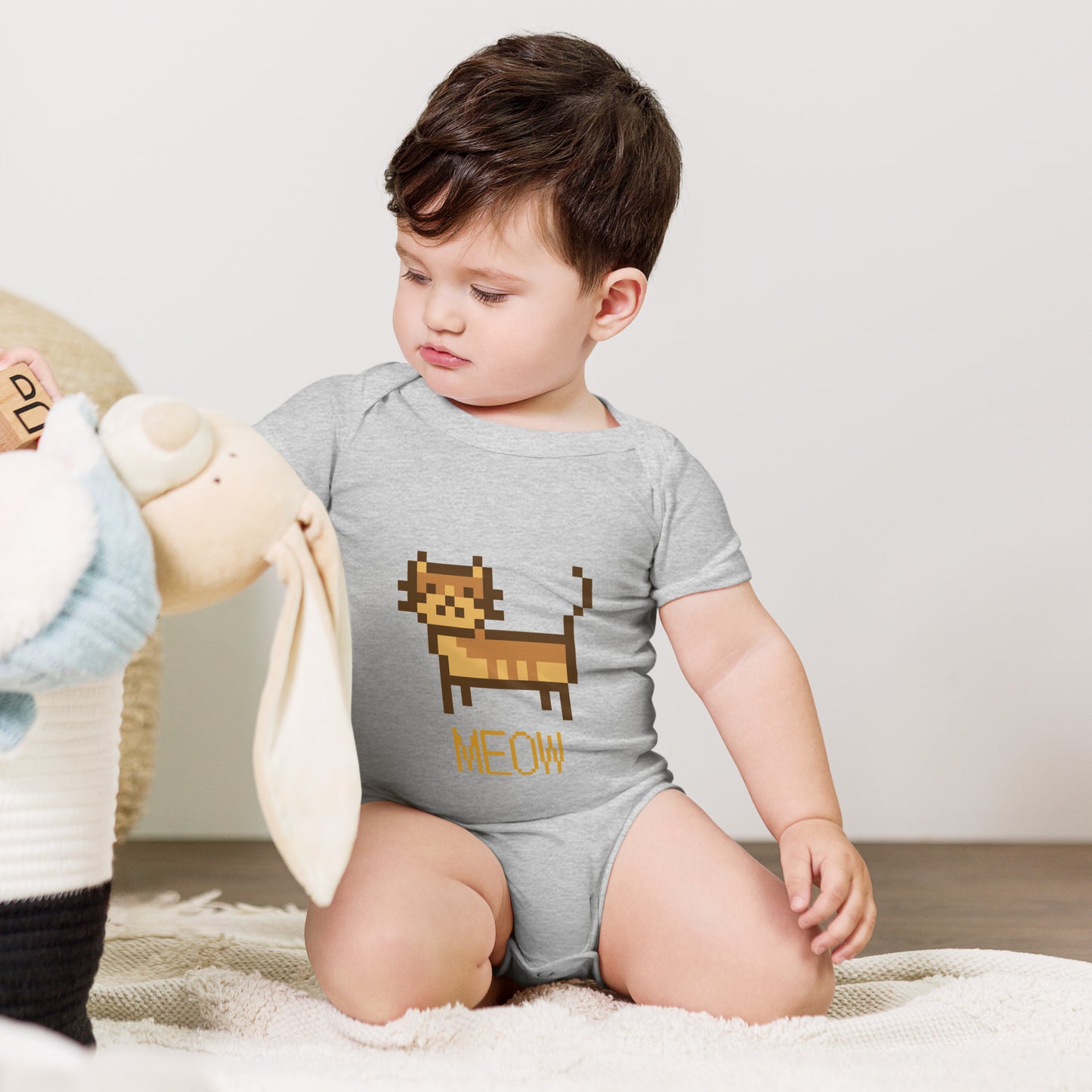 Baby with grey short sleeve one piece with a pixeled picture of a cat and the text MEOW
