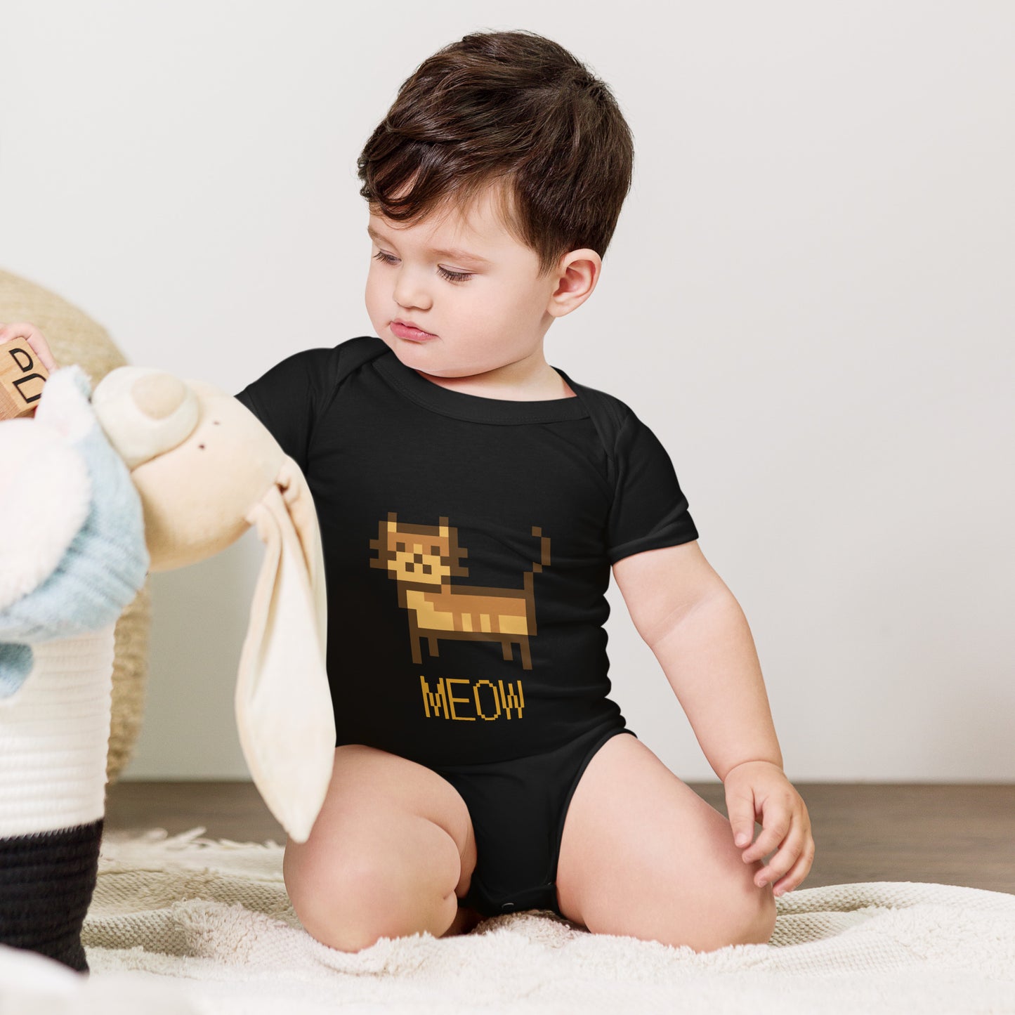 Baby with black short sleeve one piece with a pixeled picture of a cat and the text MEOW