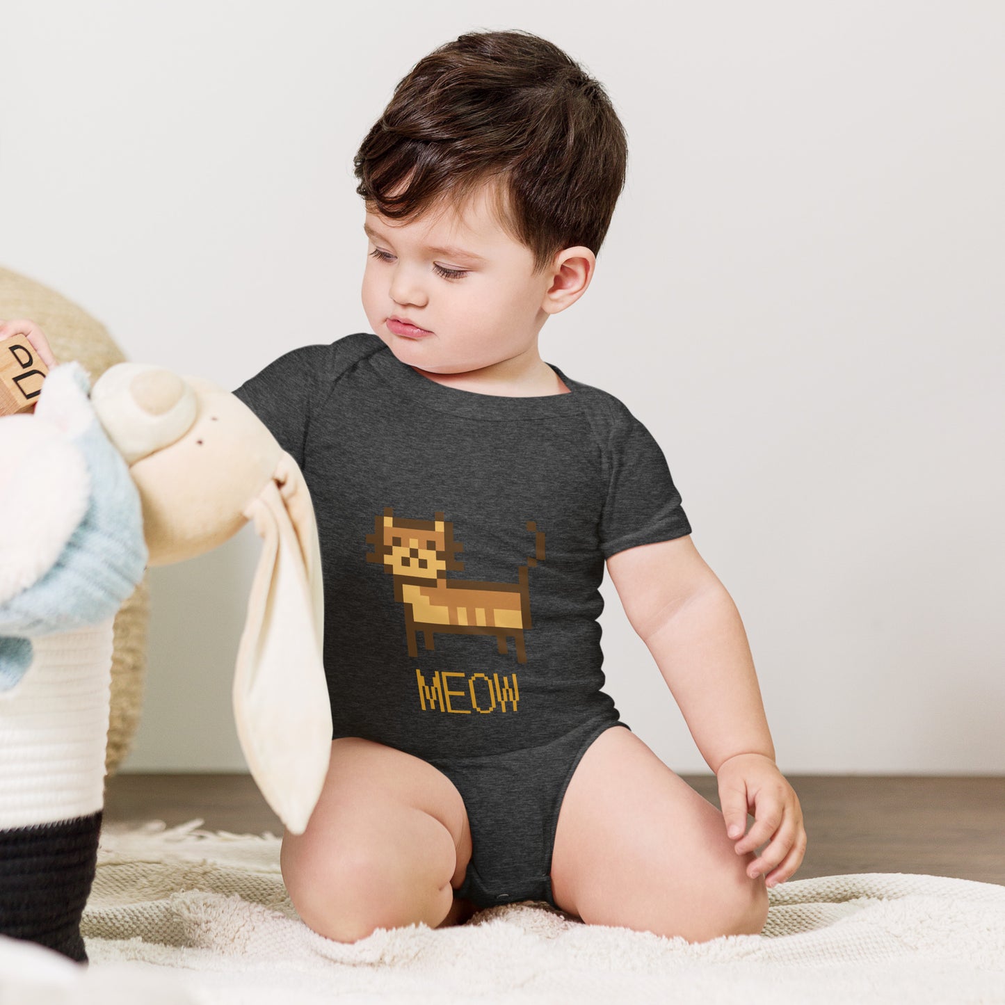 Baby with dark grey short sleeve one piece with a pixeled picture of a cat and the text MEOW