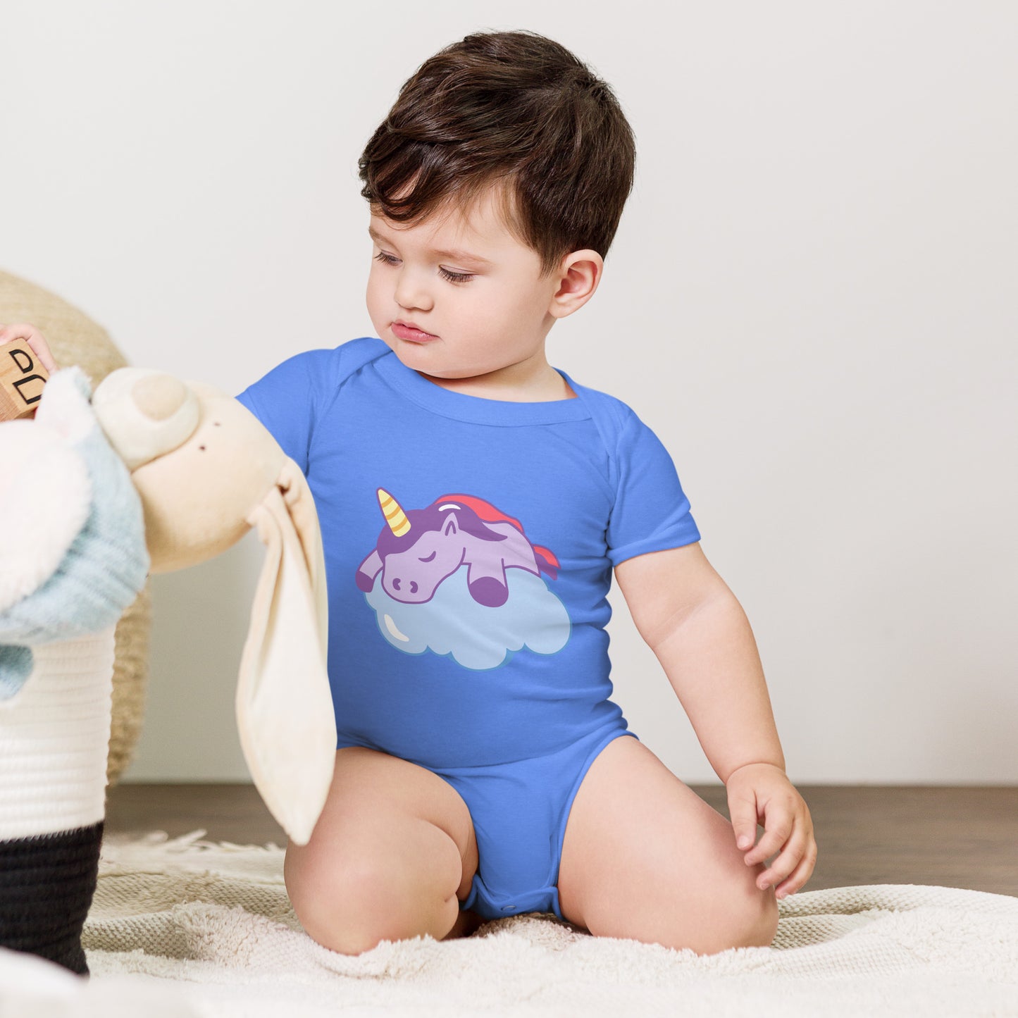 baby with a columbia blue bodysuit with a print of a sleeping unicorn on a cloud