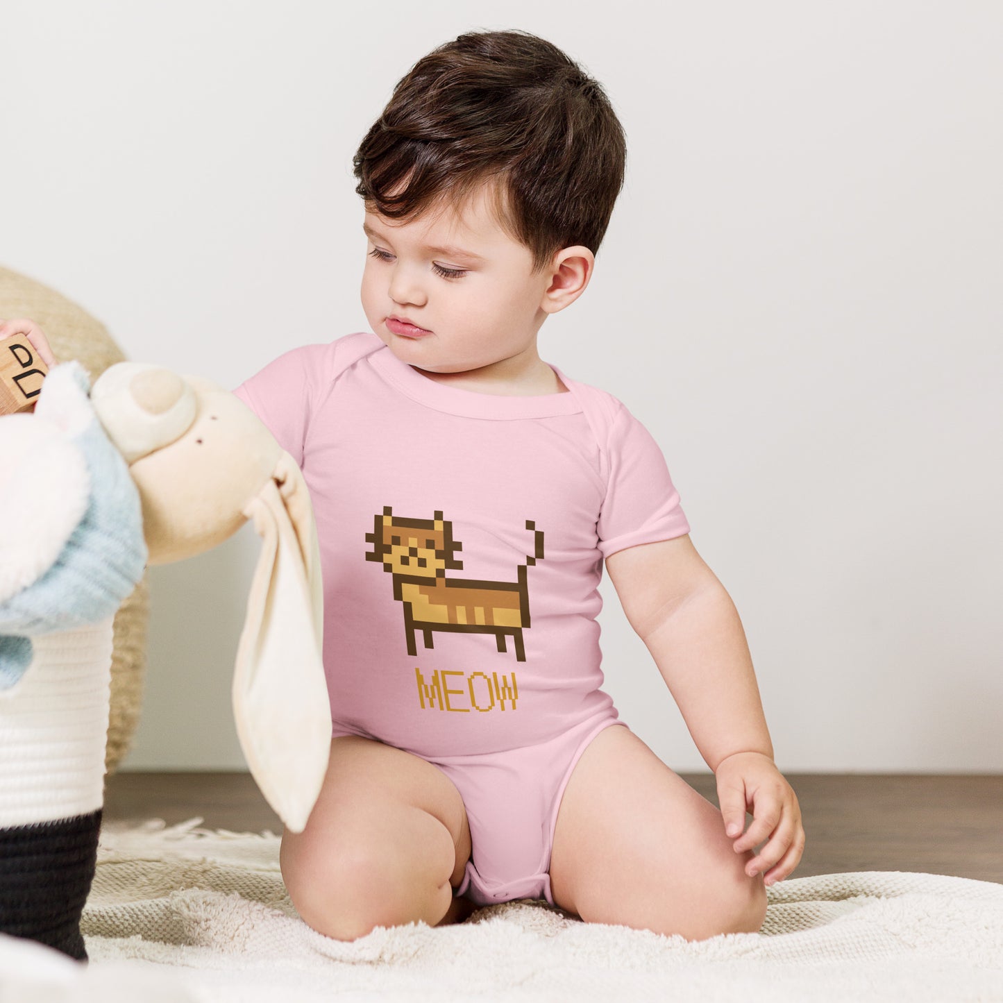 Baby with pink short sleeve one piece with a pixeled picture of a cat and the text MEOW