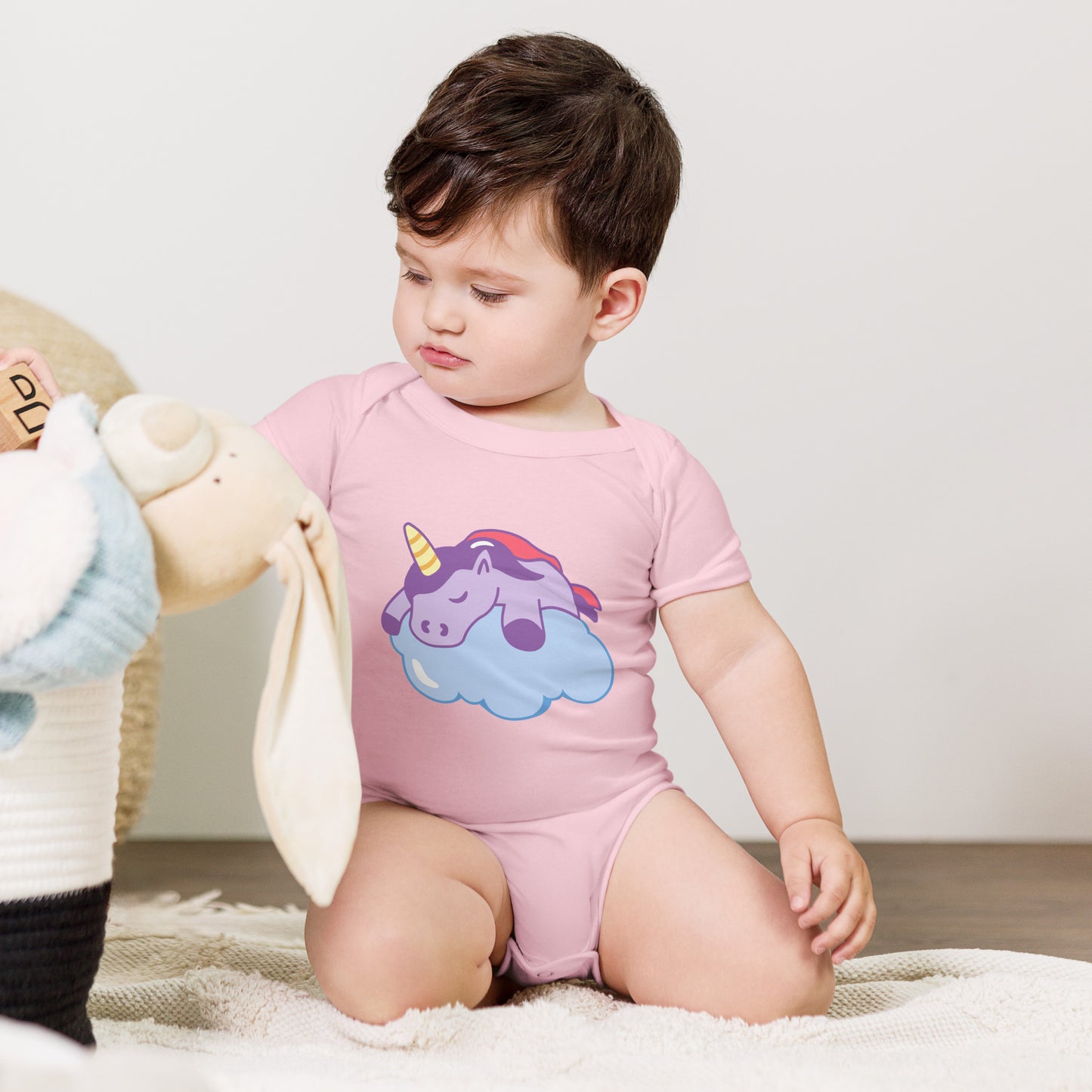 baby with a pink bodysuit with a print of a sleeping unicorn on a cloud