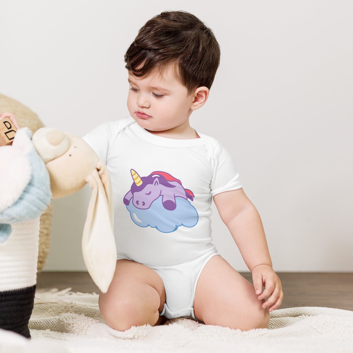 baby with a white bodysuit with a print of a sleeping unicorn on a cloud