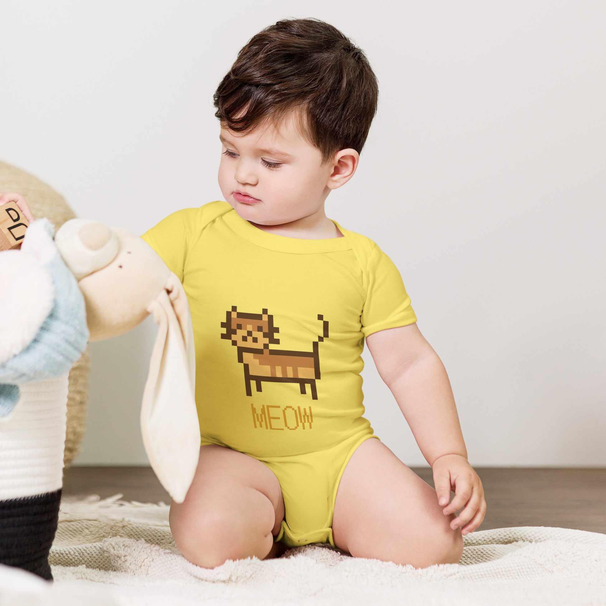 Baby with yellow short sleeve one piece with a pixeled picture of a cat and the text MEOW