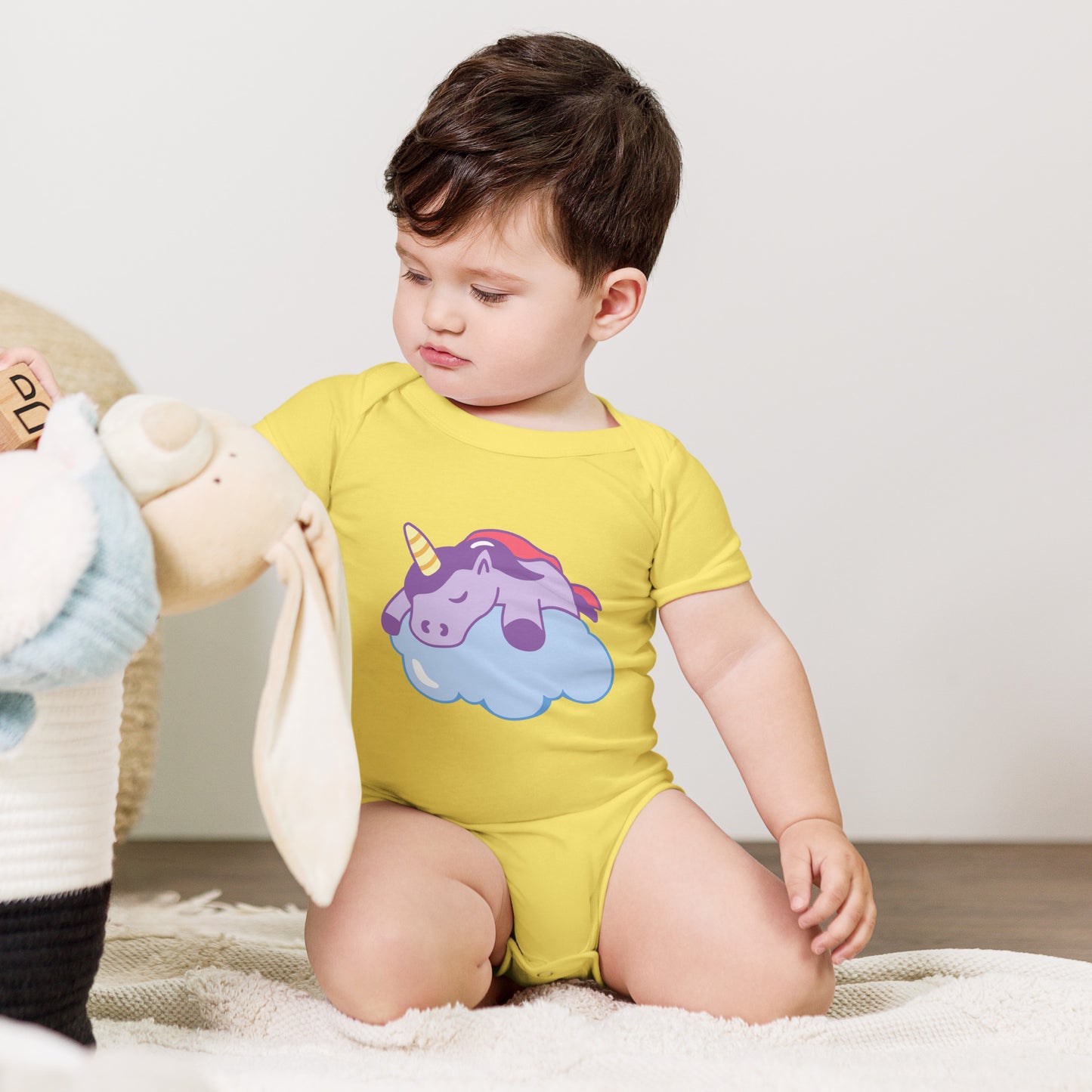 baby with a yellow bodysuit with a print of a sleeping unicorn on a cloud