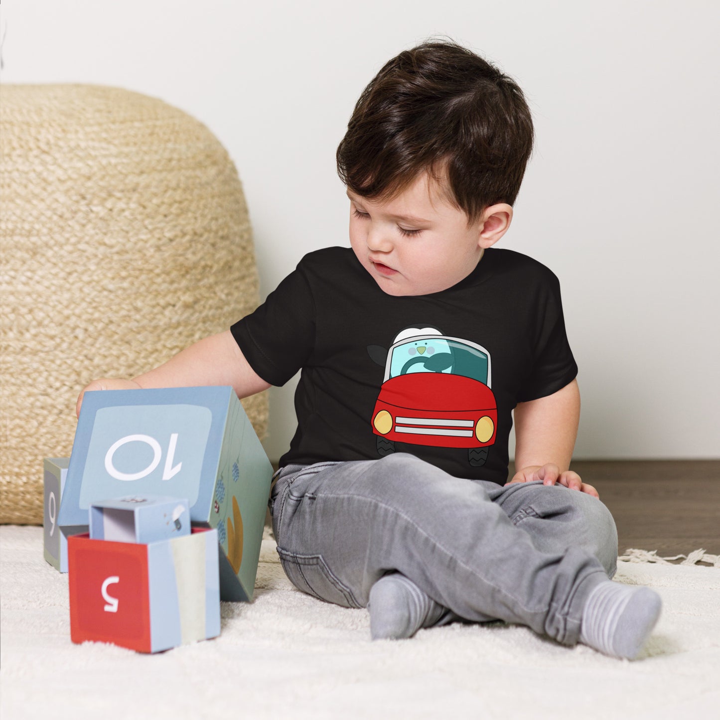 toddler with black t-shirt with picture of penguin driving a red car