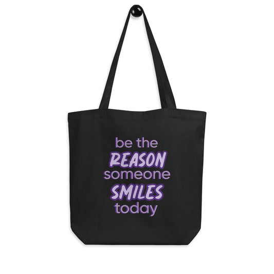 Black tote bag with the quote "be the reason someone smiles today" in purple on it. 