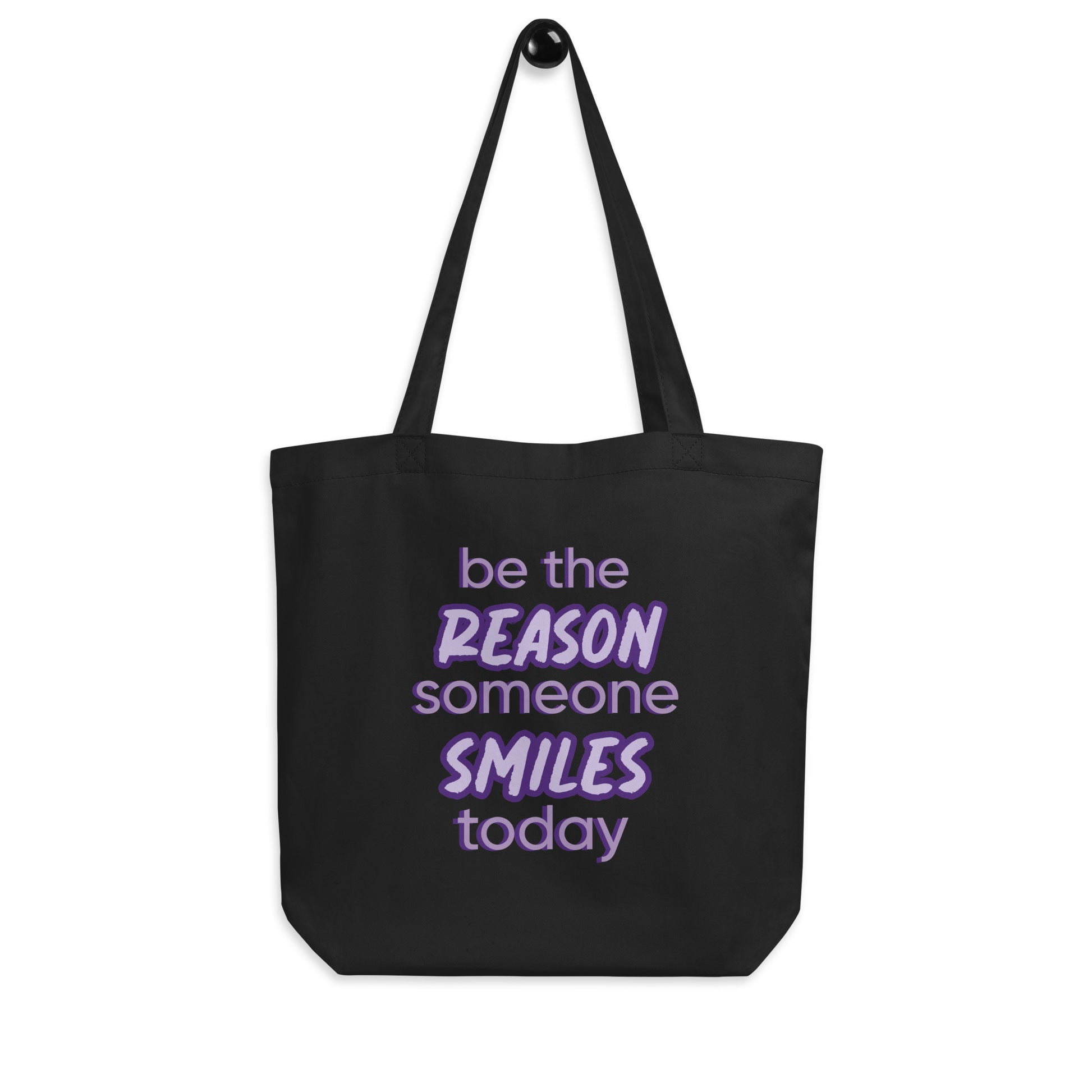 Black tote bag with the quote "be the reason someone smiles today" in purple on it. 